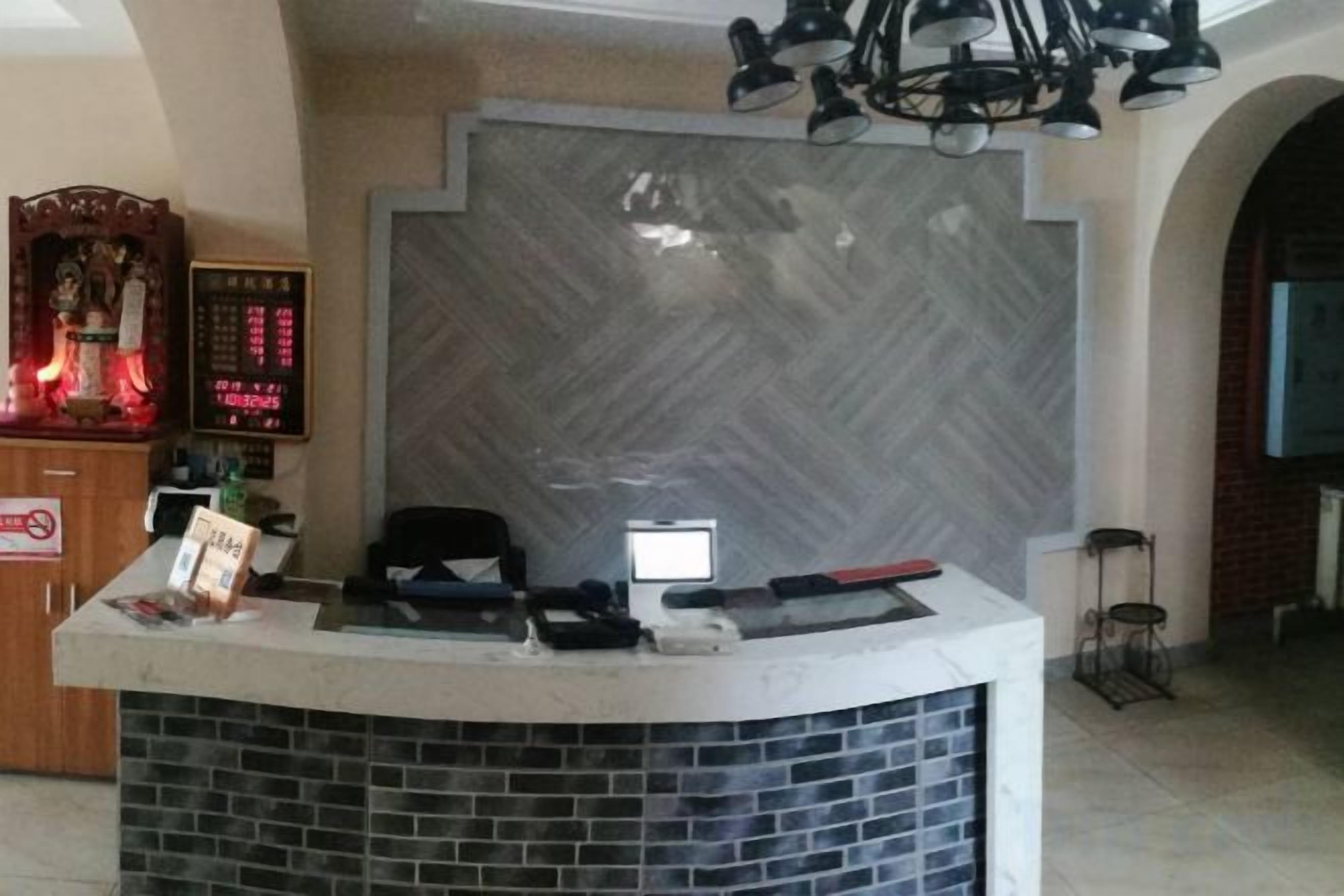 Una recepción con mostrador, pantalla digital, pared de ladrillo y candelabro.