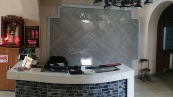Una recepción con mostrador, pantalla digital, pared de ladrillo y candelabro.