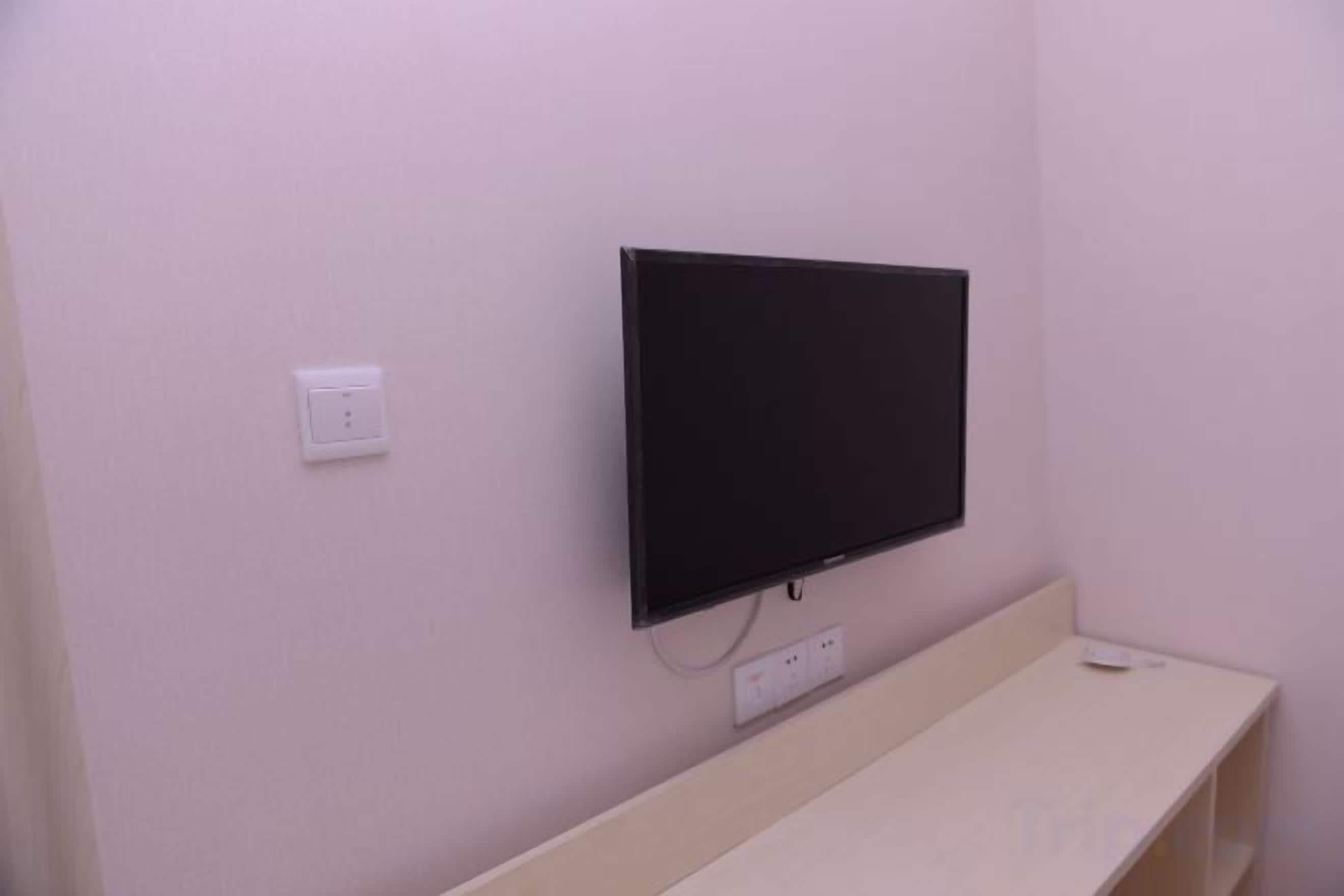 Un televisor montado en la pared, con un enchufe y un decodificador debajo.