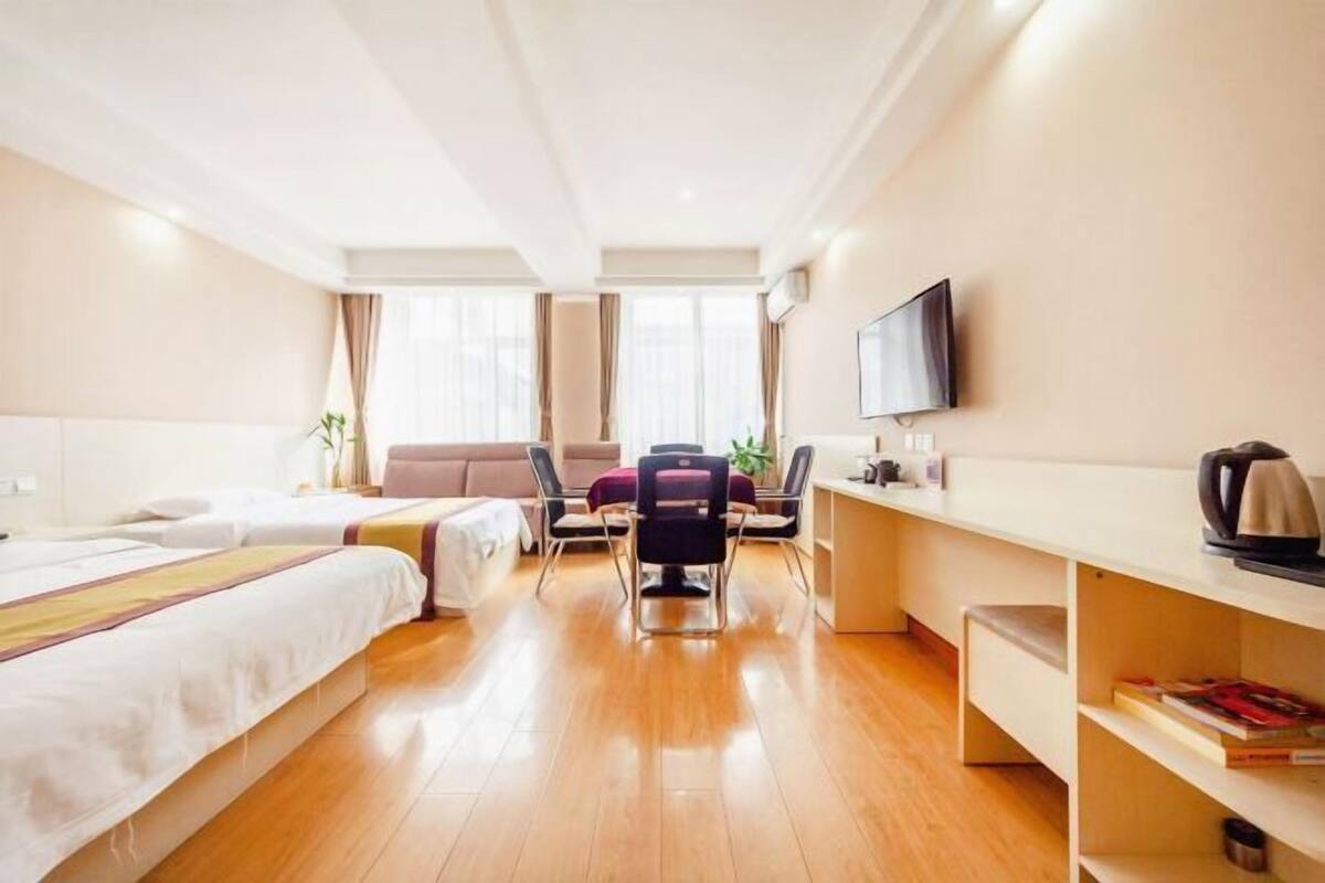 A hotel room with two beds, a desk, a chair, a TV, and a bookshelf.