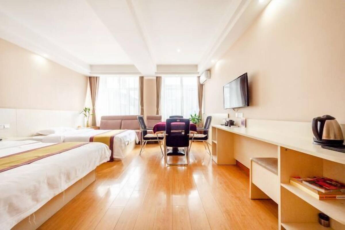 A hotel room with two beds, a desk, a chair, a TV, and a bookshelf.