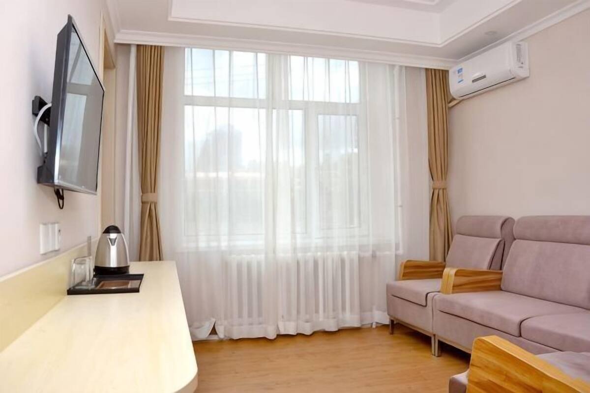 A room with a sofa, a TV mounted on the wall, a window with curtains, and a flat-screen TV.