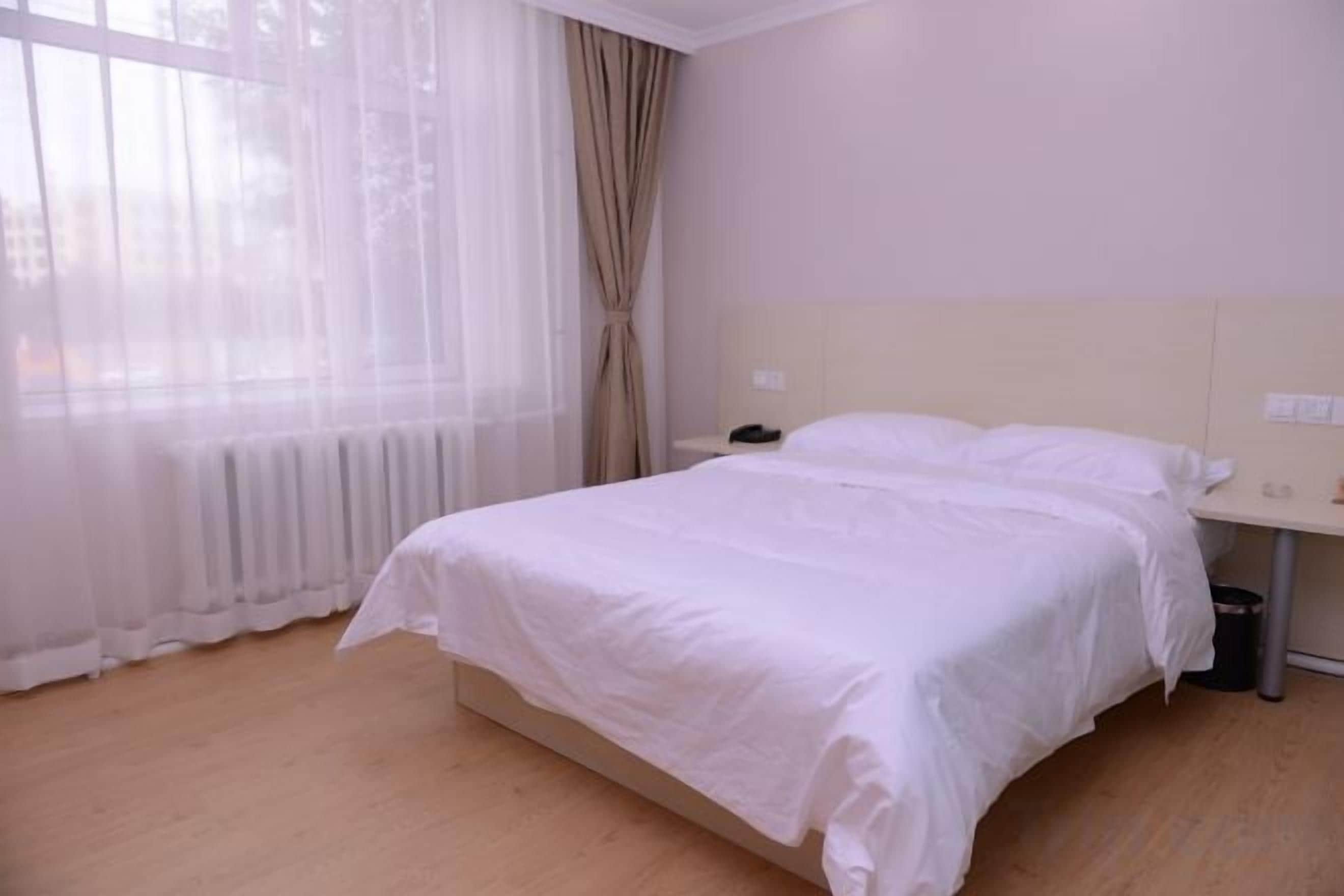 Una habitación de hotel con una cama grande, una mesita de noche y una ventana con cortinas translúcidas.