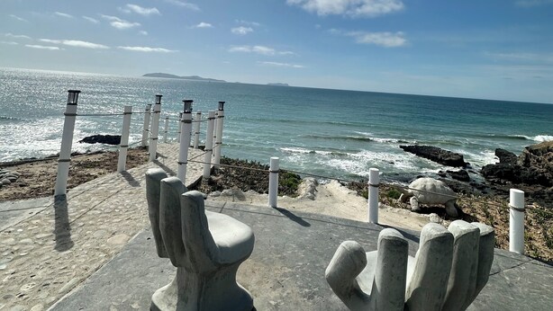 Ein Küstenweg mit Steinskulpturen und Blick auf das Meer.