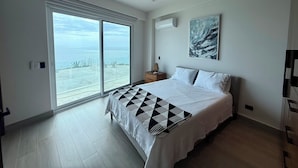 Ein Schlafzimmer mit Bett, Deckenventilator, großem Fenster mit Meerblick und einem Bild an der Wand.