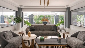A modern living room with a grey sofa, two armchairs, a coffee table, and a large window offering a view of greenery and buildings. - Luxury, pool, gym in the city center (Distrito Nacional)