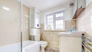 Un baño moderno con ducha envuelta en vidrio, inodoro blanco, lavamanos con dispensador de jabón y ventana que proporciona luz natural.