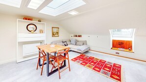 Una habitación con tragaluz, una mesa de comedor con sillas, un sofá, un ventanal con vistas y una alfombra roja estampada.