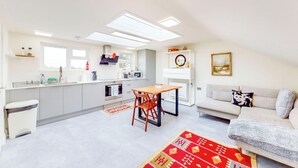 Un apartamento moderno con cocina, comedor y sala de estar. Cuenta con un ventanal grande, una lámpara de techo y un sofá con un cojín decorativo.