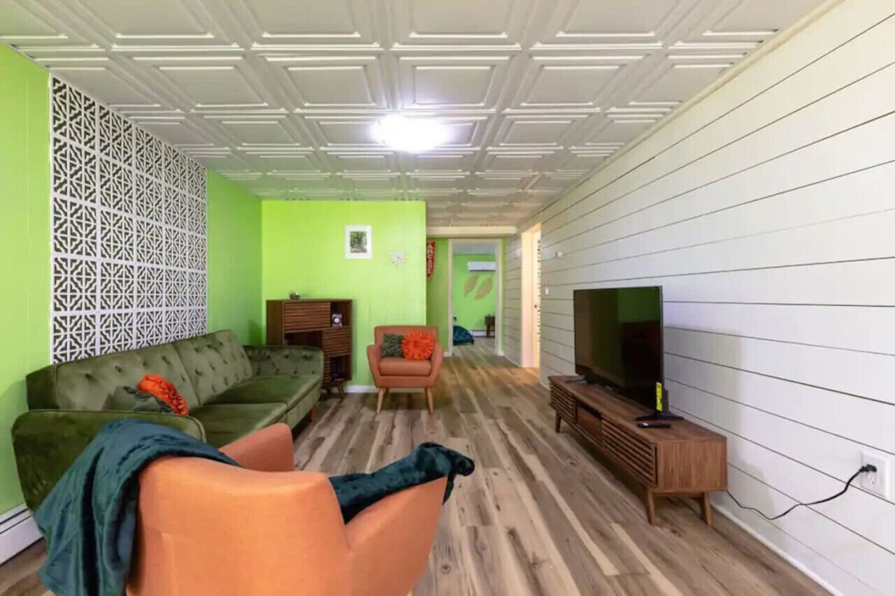 Ein Wohnzimmer mit einem grünen Sofa, einem Holztisch und einem Fernseher auf einem Schrank.