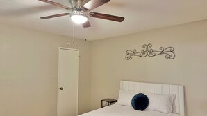 Une chambre à coucher avec un lit, un ventilateur de plafond, une porte blanche et un élément décoratif mural.