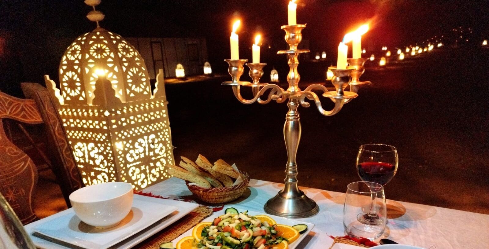 A table set for a meal with a candelabra, a bowl, a plate of food, and a glass of red wine.