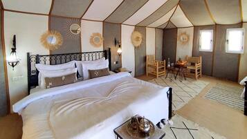 Alojamento em tenda luxuoso, com uma cama grande, vários espaços de estar e elementos decorativos nas paredes.