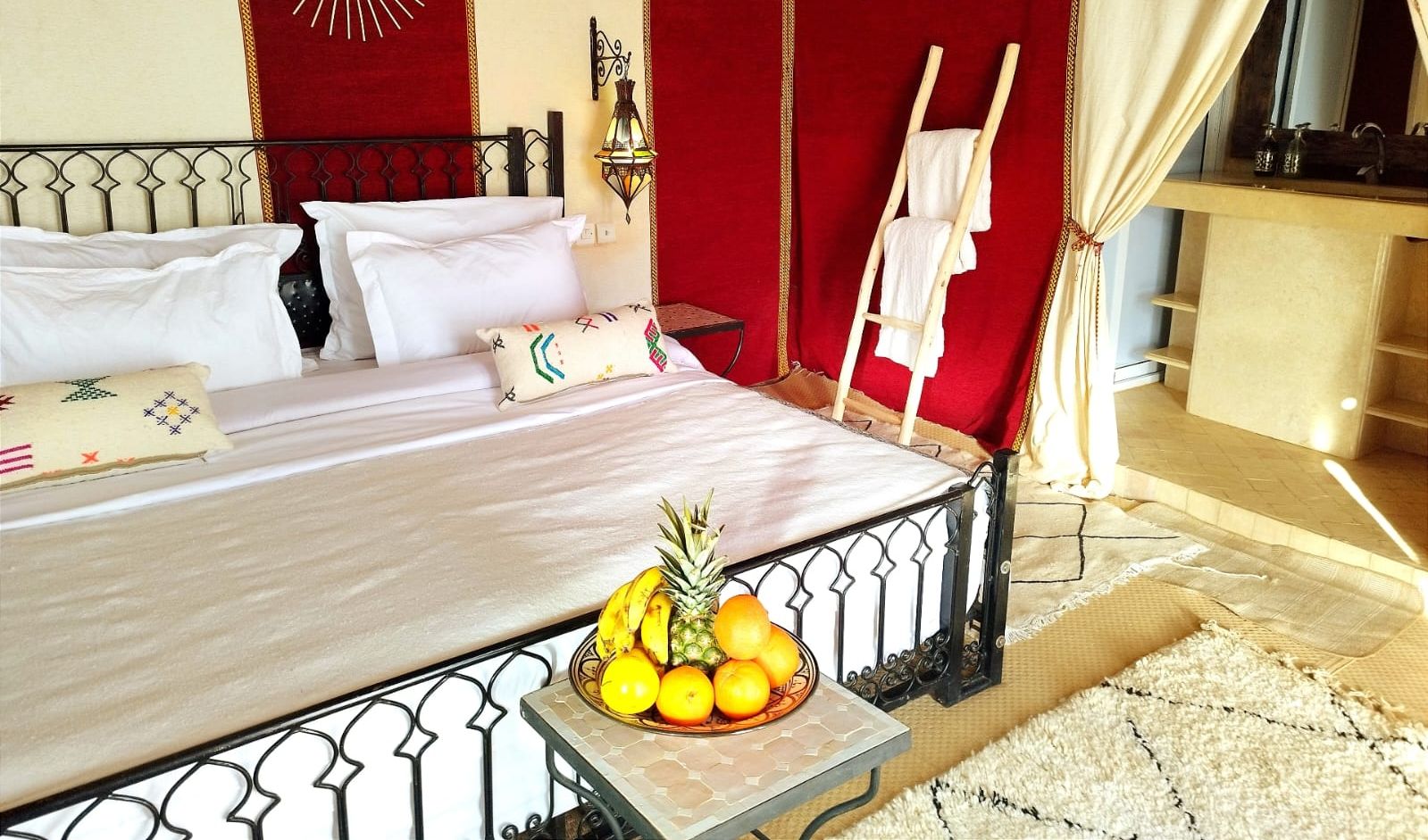 Una cama lujosa con sábanas blancas, un frutero a un lado y una cortina roja.