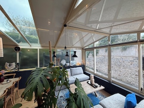 A conservatory with a dining area, seating, and a view of a stone wall.