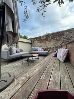 Eine Terrasse im Freien mit einer Steinwand, einer grauen Sofagarnitur und einem Holzboden.