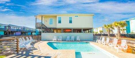 A pool area with lounge chairs and a building with a balcony.