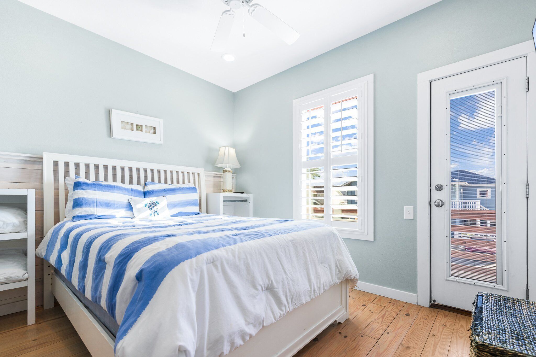 Une chambre à coucher comprenant un lit, des tables de chevet, une commode, une fenêtre avec des stores et une porte.