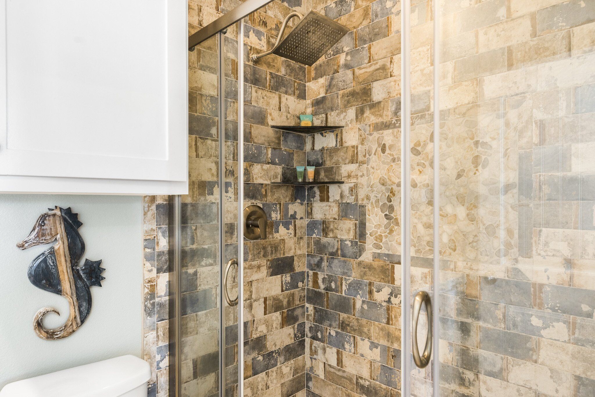 Bagno con zona doccia, parete in mosaico e porta in vetro.