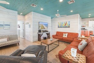 A spacious living area with a wooden ceiling, a television, and a painting of sailboats.