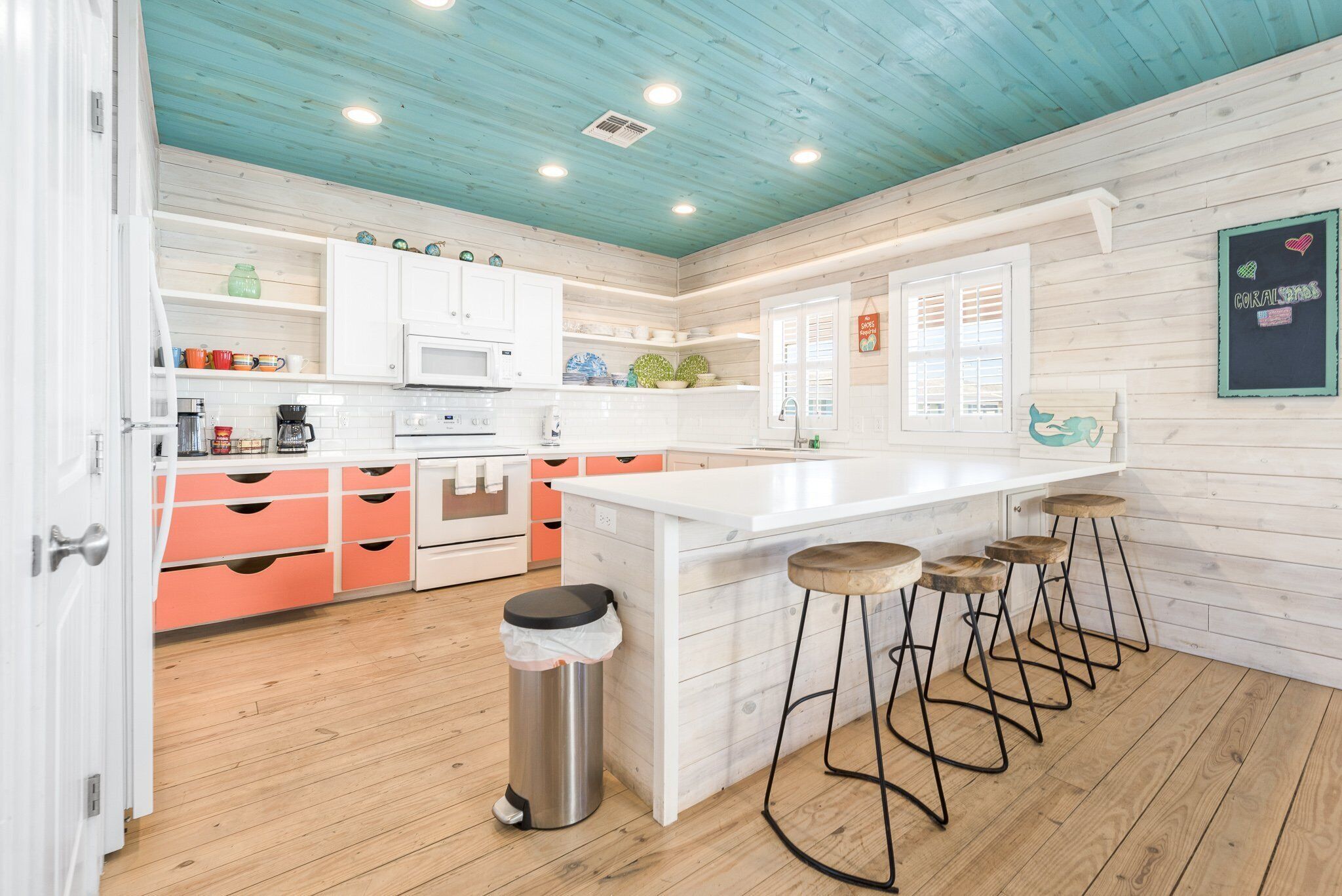 Une cuisine moderne avec des meubles blancs, un îlot central doté de tabourets et un plafond en bois.