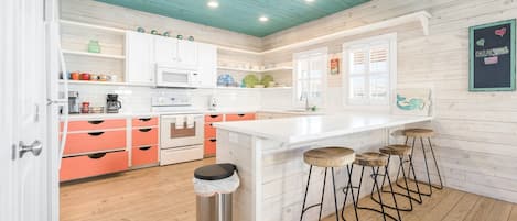 A modern kitchen with white cabinets, a central island with stools, and a wooden ceiling.