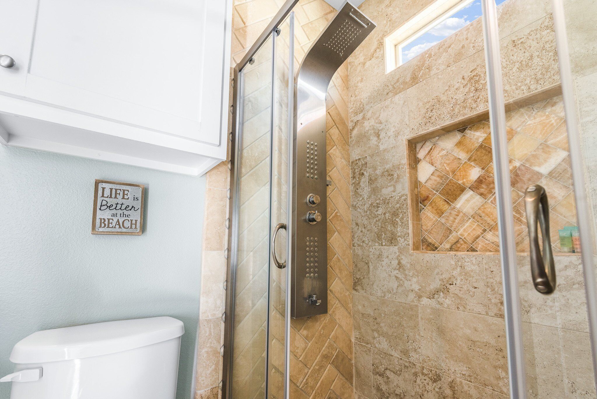 Un baño con ducha de vidrio, inodoro y un letrero en la pared que dice "LIFE is Better at the BEACH".