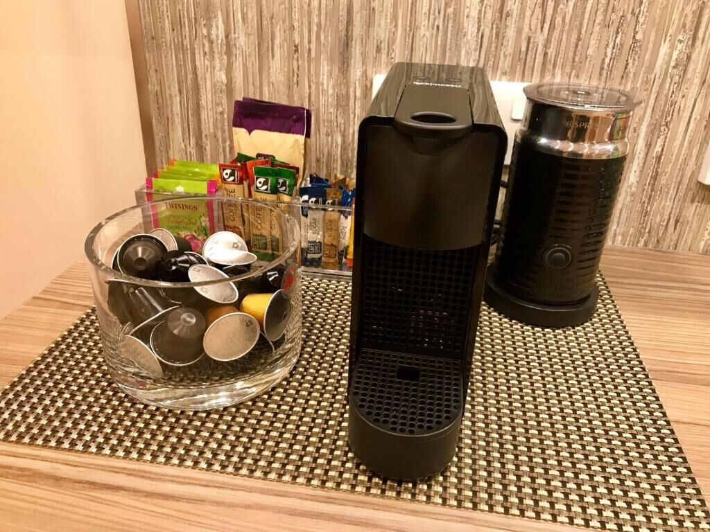 A kitchen counter with a coffee maker, a glass container with utensils, and a bag of coffee pods.