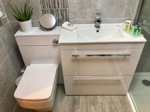 Ein modernes Badezimmer mit Toilette, Waschbecken und Pflegeutensilien sowie einer Topfpflanze.