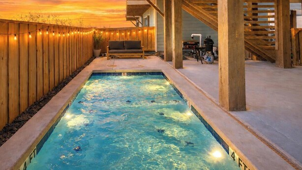 A swimming pool with a wooden deck, a bench, and a view of the sunset.