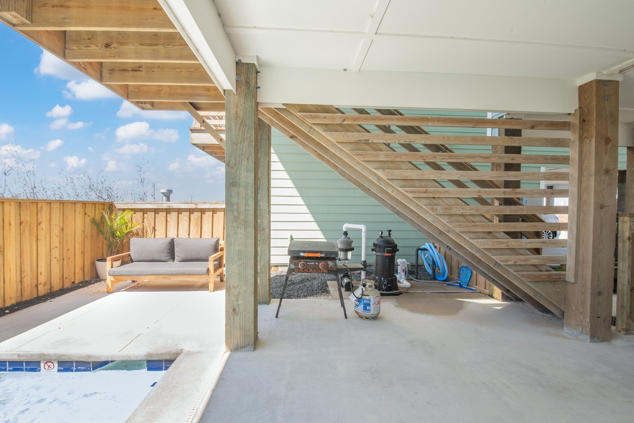 A covered outdoor area with a pool, wooden deck, and a grill.