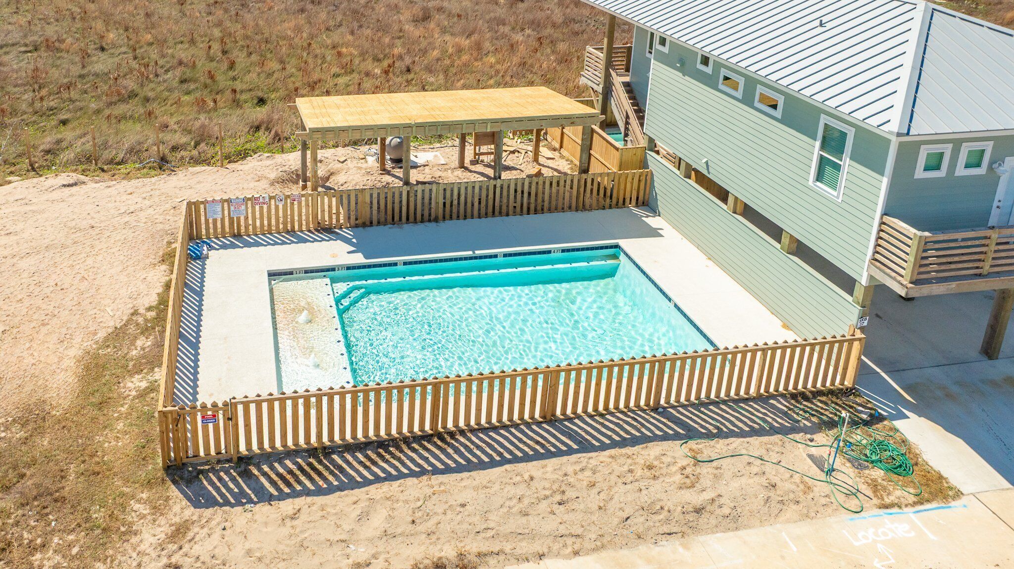 A swimming pool with a wooden deck and a covered seating area, surrounded by a wooden fence.