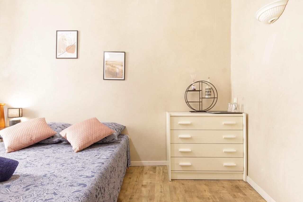 A bedroom with a bed, two pillows, a dresser, and two framed pictures on the wall.
