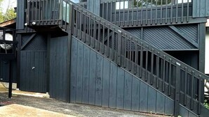 Un bâtiment moderne à l’extérieur sombre, avec un escalier menant à un balcon et de grandes fenêtres.
