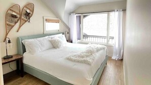 Une chambre à coucher avec un lit, un plancher en bois, une fenêtre avec des rideaux et un luminaire fixé au mur.