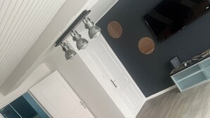 Un salon moderne avec un canapé gris, des coussins jaunes, une table basse en verre et un mur d’accent de couleur foncée.