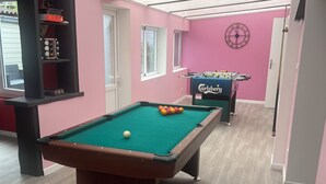 Une table de billard avec des billes, une table de baby-foot et une horloge au mur.