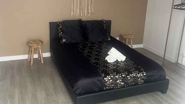 Une chambre avec un lit noir, un plancher en bois et une décoration en macramé accrochée au mur.