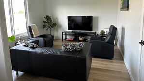 Moderni olohuone, jossa on suuri litteänäyttöinen televisio, kaksi mustaa nahkasohvaa, sohvapöytä ja kattotuuletin.