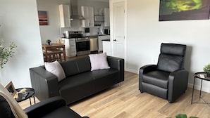 A modern living room with a black leather sofa, a black leather armchair, and a dining area with wooden furniture.