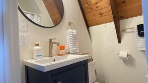 A bathroom with a wooden ceiling, a white sink, a mirror, and a toilet. - Honest Abe Frame @ Sunrise (Ellicottville)