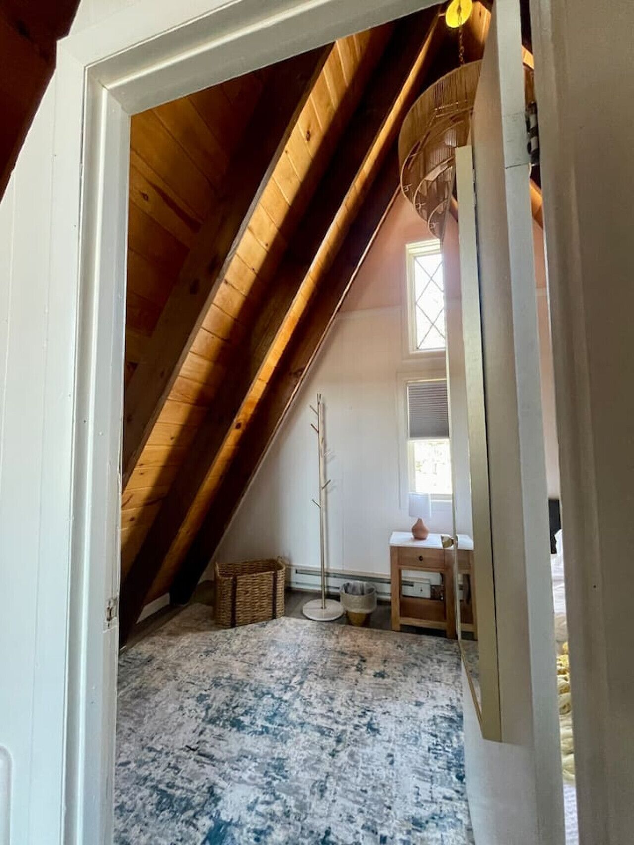 Una stanza mansardata con travi in legno a volta, una lampada da terra, un tavolino e una finestra.