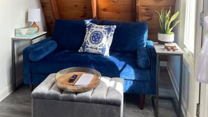 A cozy room with a blue sofa, a grey ottoman, a small side table with a lamp, and a potted plant. - Honest Abe Frame @ Sunrise (Ellicottville)
