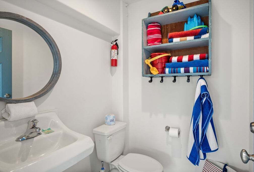 A bathroom with a white sink, toilet, and a shelf with towels and a fire extinguisher.