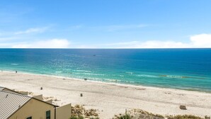 A beach with a clear view of the ocean, a sandy shore, and a building in the foreground. - Prancing Peacock Gulf View Condo (Panama City Beach)