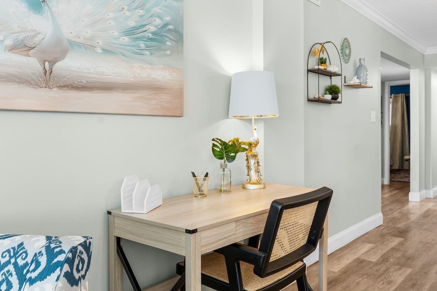 A dining area with a wooden table, a black chair, a white lamp, and a painting of a peacock.
