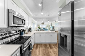 A modern kitchen with stainless steel appliances, white cabinetry, and a central island. - Prancing Peacock Gulf View Condo (Panama City Beach)