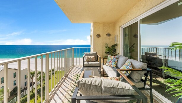 A balcony with a view of the ocean, furnished with a sofa, armchairs, and a coffee table. - Prancing Peacock Gulf View Condo (Panama City Beach)