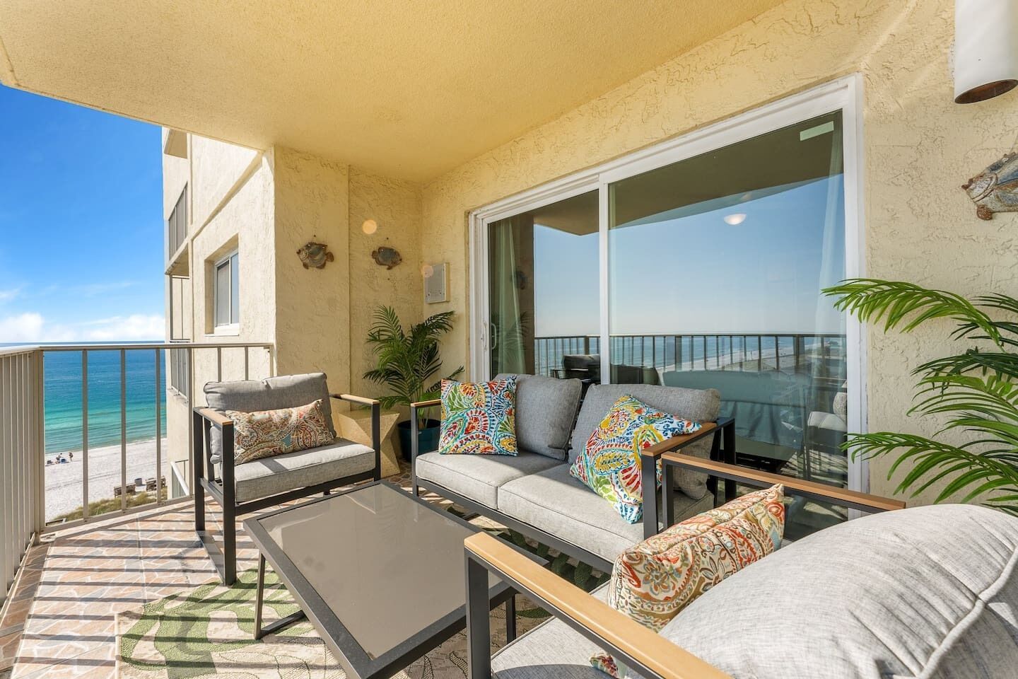 A balcony with a sofa, two armchairs, and a coffee table. There is a view of the ocean and a building across the street.