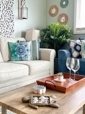 Sala de estar com sofá bege, almofadas decorativas, mesa de centro de madeira com bandeja e uma planta em vaso.